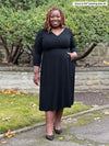 Miik model plus size Erica (5'8", 2X) smiling wearing Miik's Lolly midi flounce dress with pockets in black 