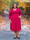 Miik model plus size Sureka (5'9", 3x) smiling wearing Miik's Lolly midi flounce dress with pockets in bordeaux