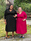 Miik model plus size Kimesha and Jennifer standing next to each other smiling both wearing Miik's Lolly midi flounce dress with pockets. Kimesha is wearing the dress in black and Jennifer in bordeaux 