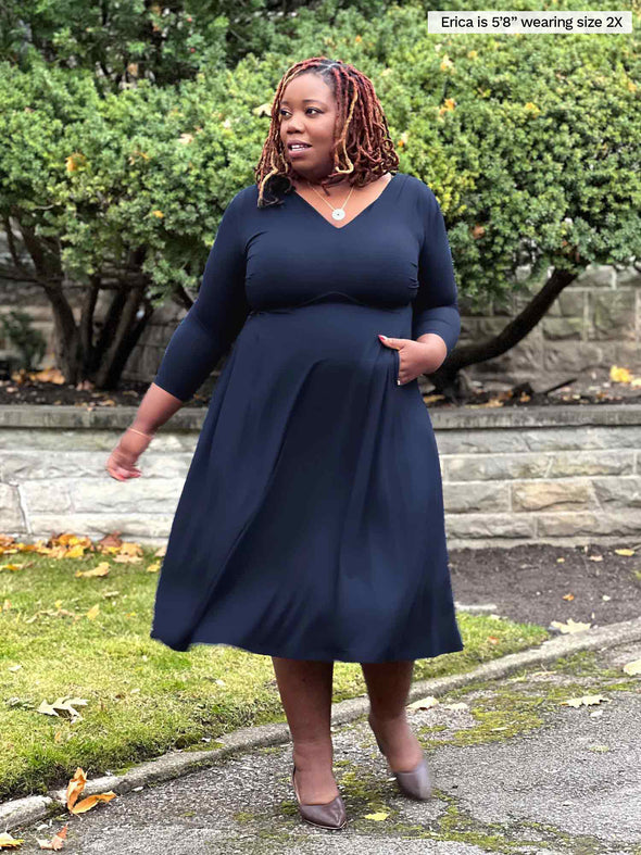 Miik model plus size Erica (5'8", 2x) looking away wearing Miik's Lolly midi flounce dress with pockets in navy