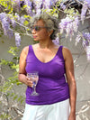 Woman standing in a garden looking away and holding a glass of water wearing Lori reversible slouchy tank top in grape with a white pant