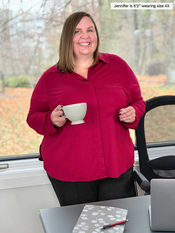Miik model plus size Jen (5'2", 4x) smiling while standing next to a office desk holding a mug wearing Miik's Lucia collared shirt in bordeaux 