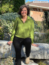 Miik founder Donna (5'6", small) sitting on a rock and looking away wearing Miik's Lucia collared shirt in green moss with a black pant and boots