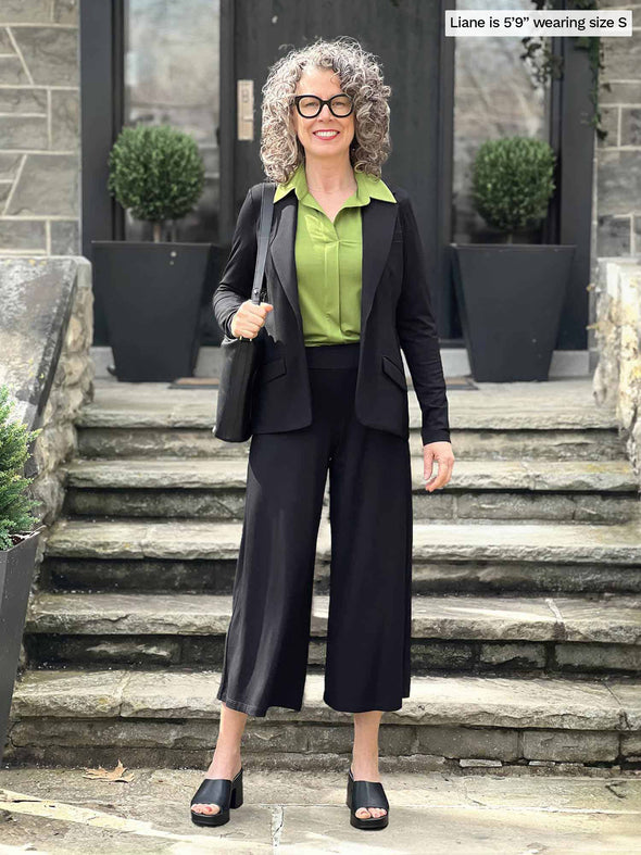 Miik model Liane (5'9", small) smiling wearing a black pant and blazer along with Miik's Lucia collared shirt in green moss
