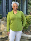 Miik model Keethai (5'5'", medium) smiling wearing Miik's Lucia collared shirt in green moss and a white jeans