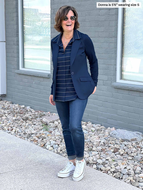 Miik model Johanna (five foot six, size extra small) smiling in front of a building wearing Miik's Lucia collared shirt in navy wide pinstripe with a white jeans