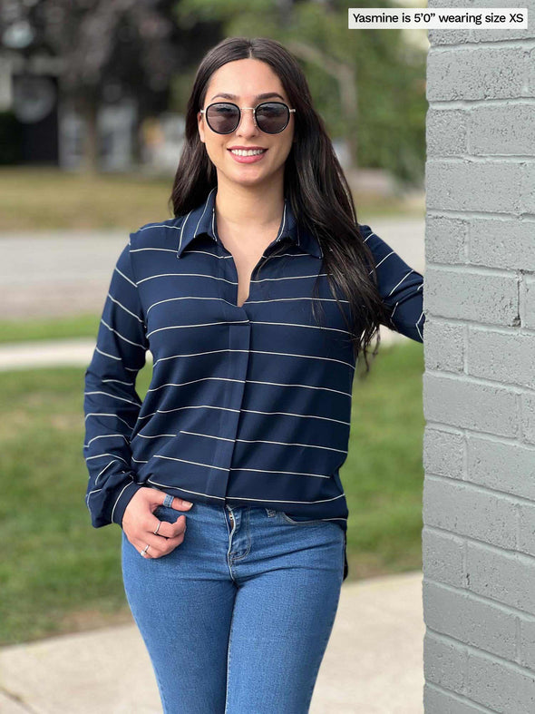 Woman standing next to a brick wall wearing Miik's Lucia collared shirt in navy pinstripe with jeans and sunglasses