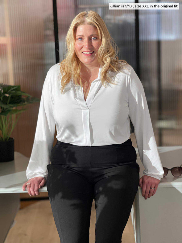 Miik model Jillian (5'10", xxlarge) leaning against to a office desk wearing a black pant with Miik's Lucia collared shirt in white in the original fit tucked in 