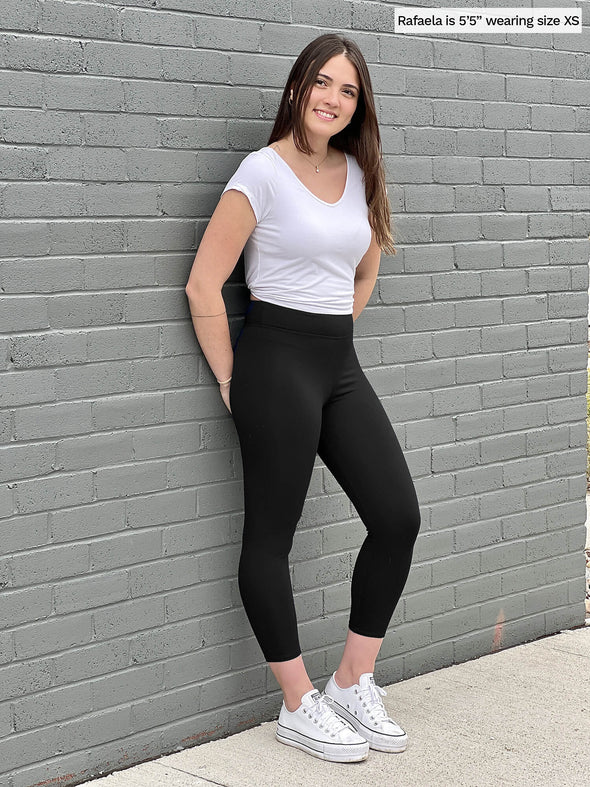 Woman standing in front of a brick wall wearing Miik's Lucy capri legging in black with a white basic t-shirt