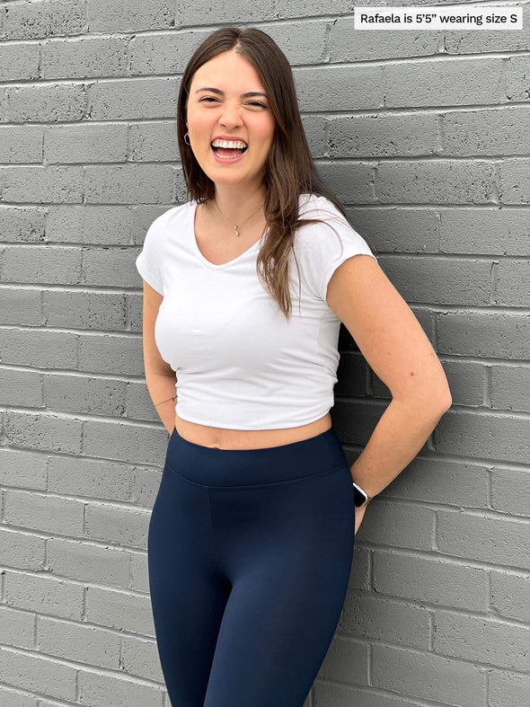 Woman smiling and standing in front of a brick wall wearing Miik's Lucy capri legging in navy with a cropped t-shirt in white