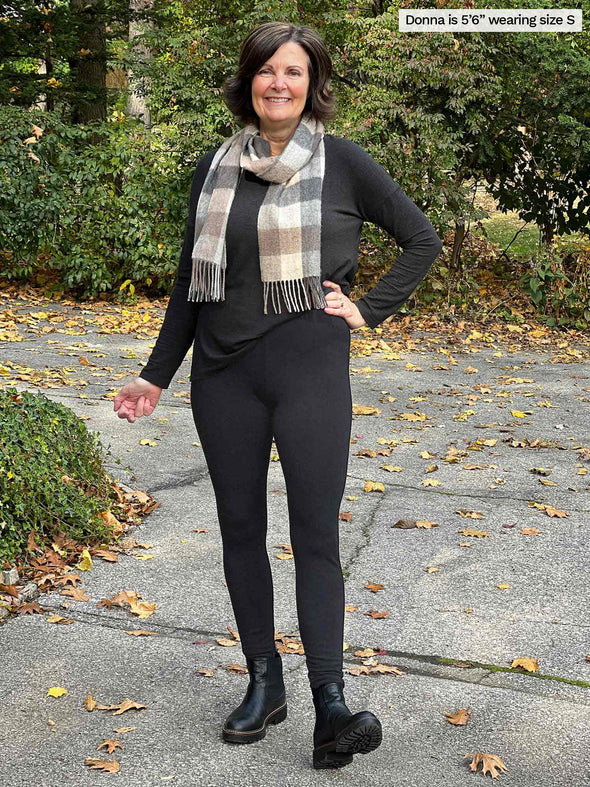 Miik founder Donna (5'6", small) smiling white standing outside wearing Miik's Lucy mid-rise legging in charcoal with a long sleeve tee in the same colour and a scarf in earth neutral tones 