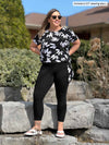 Miik model Christal (5'3", large) smiling and looking away wearing Miik's Lucy mid-rise capri legging in black with a printed top in white lily