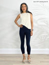 Miik model Lisa (5'6", xsmall) standing in front of a white wall wearing Miik's Lucy mid-rise capri legging in navy along with a natural tank top