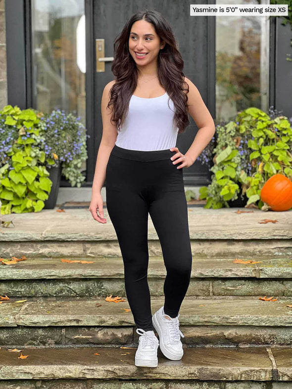 Miik model Yasmine (5'0", xsmall) wearing Miik's Lucy mid-rise legging in black with a white tank top and sneakers.