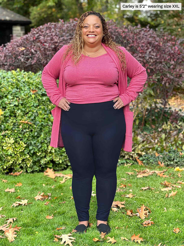 Miik model Carley (5'2", xxlarge) smiling while standing on grass wearing Miik's Lucy mid-rise legging in navy along with a pink pomegranate melange top and a cardigan in the same colour