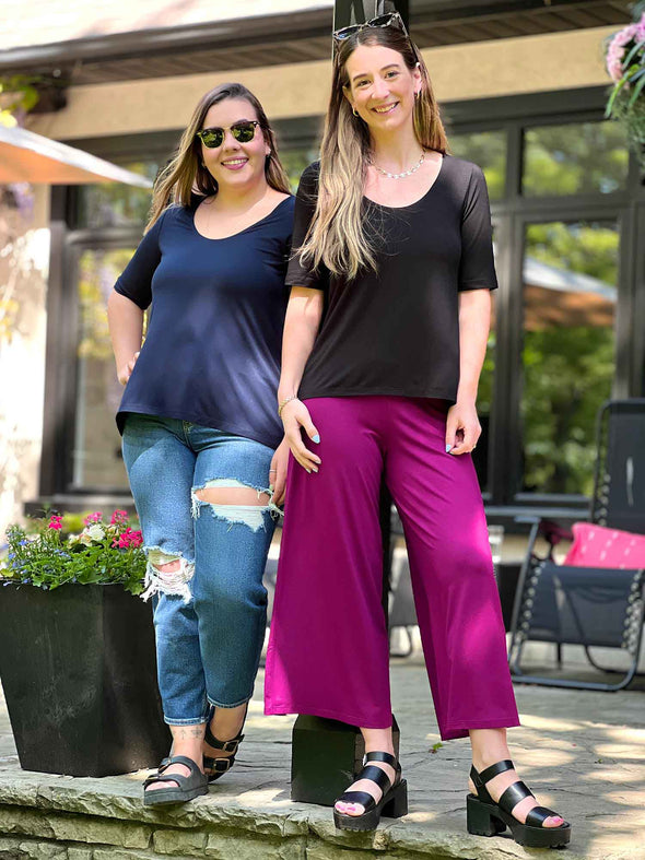 Miik models Johanna and Christal standing next to each other and smiling while both wearing Miik's Luisa half sleeve high low top in black and navy