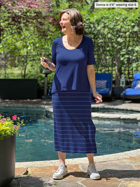Miik founder Donna (five feet six, small) standing in front of a poo, laughing and looking away wearing Miik's Luisa half sleeve high low top in navy along with a pinstripe navy midi skirt