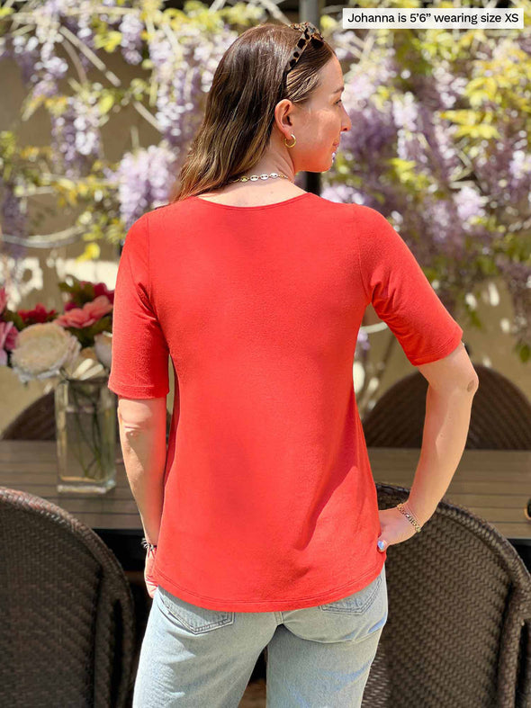 Miik model Johanna (five feet six, size xsmall) standing with her back towards the camera showing the back of Miik's Luisa half sleeve high low top in papaya melange 