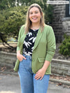 Woman standing in front of a house wearing Miik's Maeva LightLuxe washable blazer in moss green over a floral top and jeans.