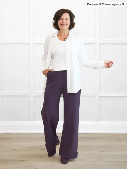 Woman wearing a white top and purple pants against a white background 