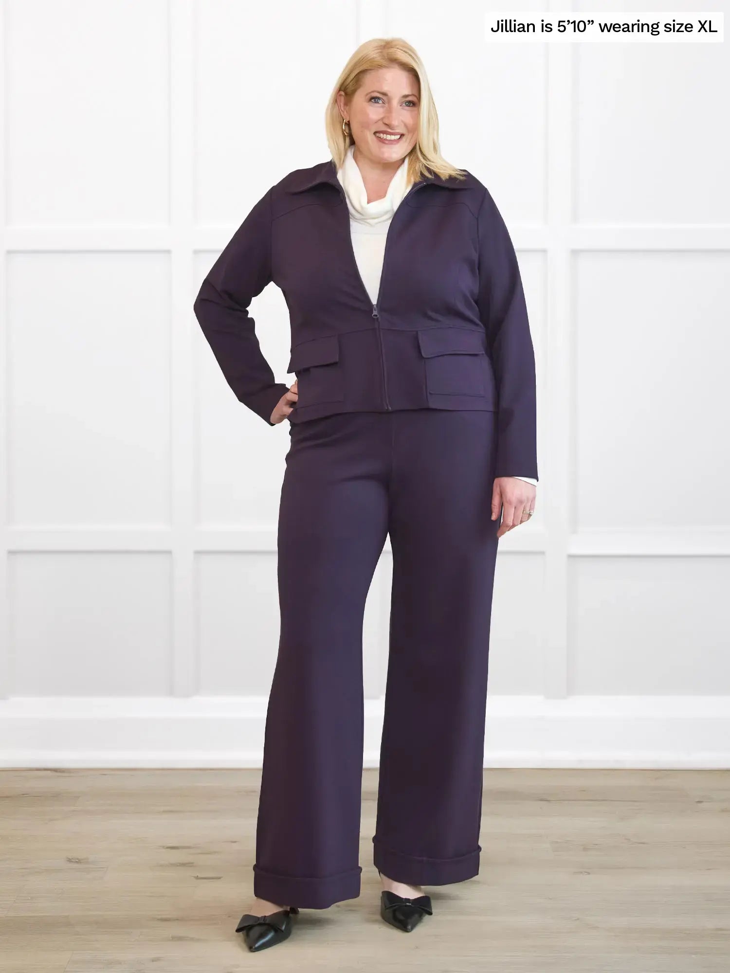 Woman wearing a purple suit standing against a white wall. 