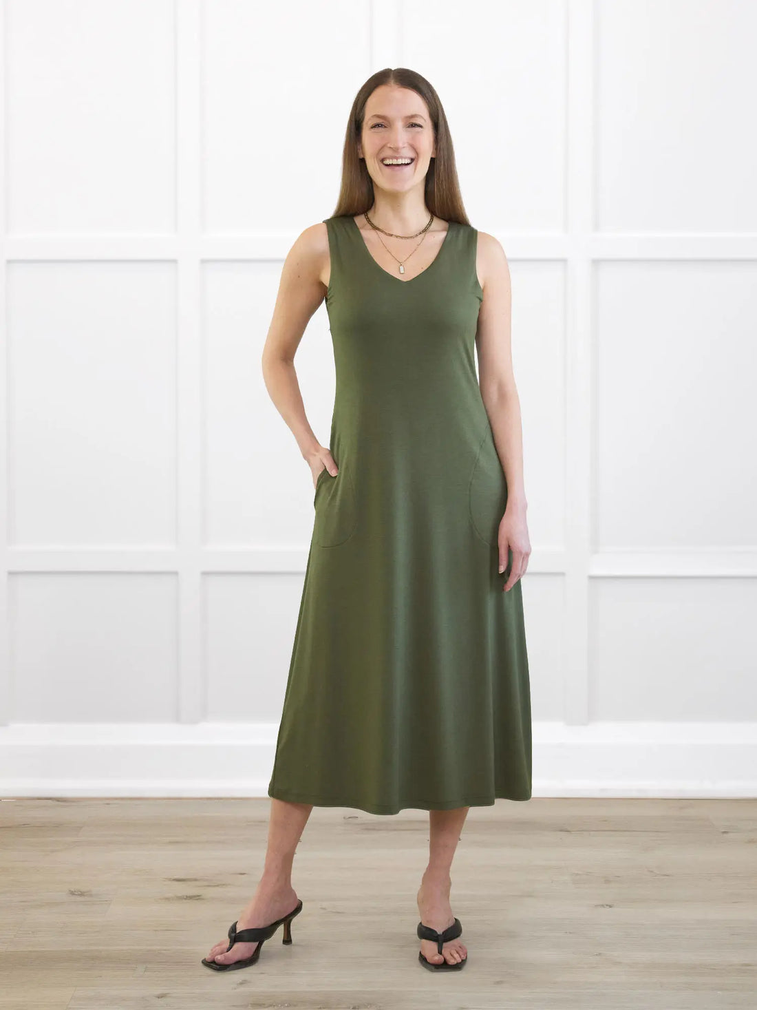 Woman wearing a green dress standing in a room with white walls and wooden floor. 