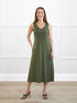 Woman wearing a green dress standing in a room with white walls and wooden floor. 