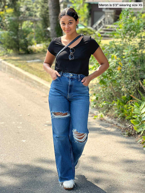 Miik model Meron (five feet three, xsmall) standing in a sidewalk wearing Miik's Marianna reversible classic tee in black tucked in a high waisted ripped jeans 