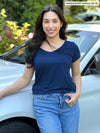 Miik model Yasmine (five feet tall, xsmall, petite) smiling while standing in front of a white car wearing Miik's Marianna reversible classic tee in navy
