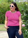 Miik model Christal (5'3". large) smiling and looking away wearing Miik's Marianna reversible classic tee in pretty in pink with navy pants 