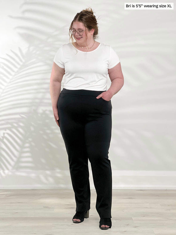 Miik model Bri (5'5", xlarge) smiling and looking down wearing Miik's Marianna reversible classic tee in white tucked in a black pant 