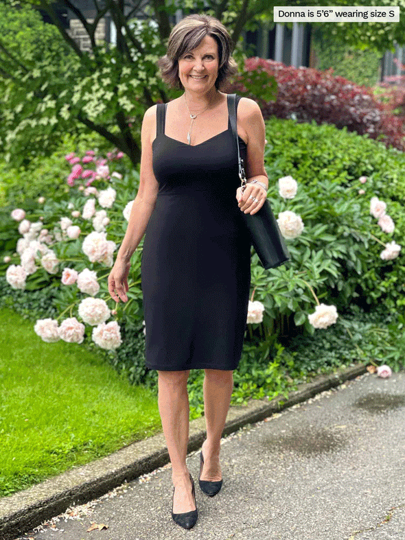 Miik founder Donna (five feet six, small) standing in front of a garden smiling wearing Miik's Maryse reversible sweetheart dress in black with a purse and shoes in the same colour