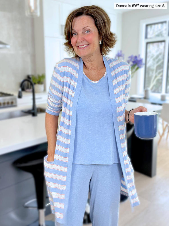 Woman smiling wearing Miik's Melanie classic cardigan with pockets in denim peony stripe with her Selena PJ set in denim melange holding a blue mug