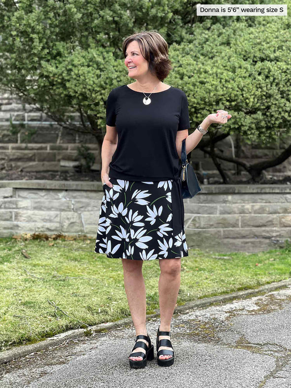 Miik founder Donna (5'6", small) smiling looking away wearing Miik's Melody side tie top in black with a printed flouncy skirt and black sandals 