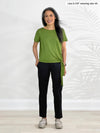 Miik model Lisa (5'6", xsmall) smiling while standing in front of a white wall wearing Miik's Melody side tie top in green moss and a black pant 