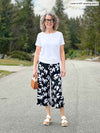 Miik model Liane (5'9", small, tall) wearing Miik's Melody side tie top in white along with a printed wide leg capri pant 