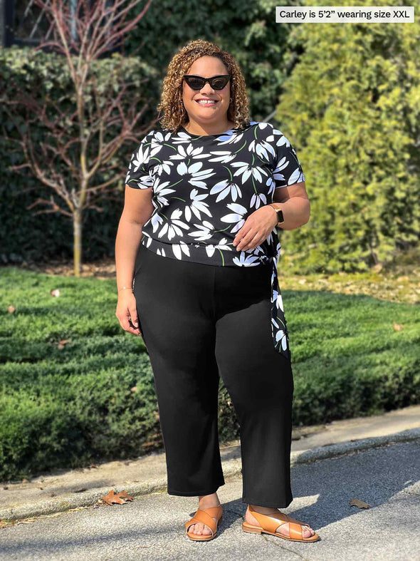 Miik model Carley (5'2". xxlarge) smiling wearing Miik's Melody side tie top in white lily along with a black capri pant