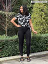 Miik model Meron (5'3", xsmall) looking away wearing a black legging along with Miik's Melody side tie top in white lily