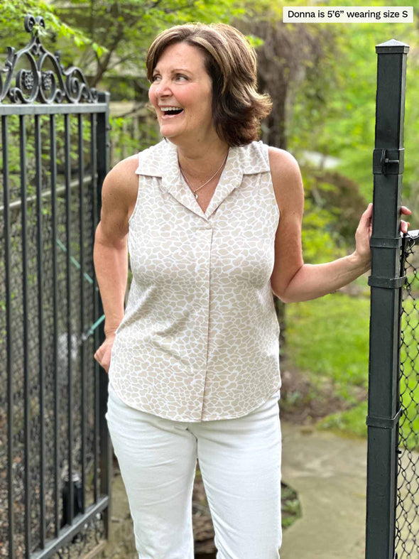 Miik founder Donna (five feet six, small) standing next to a gate looking away wearing Miik's Mika sleeveless collared shirt in cobblestone print with white jeans