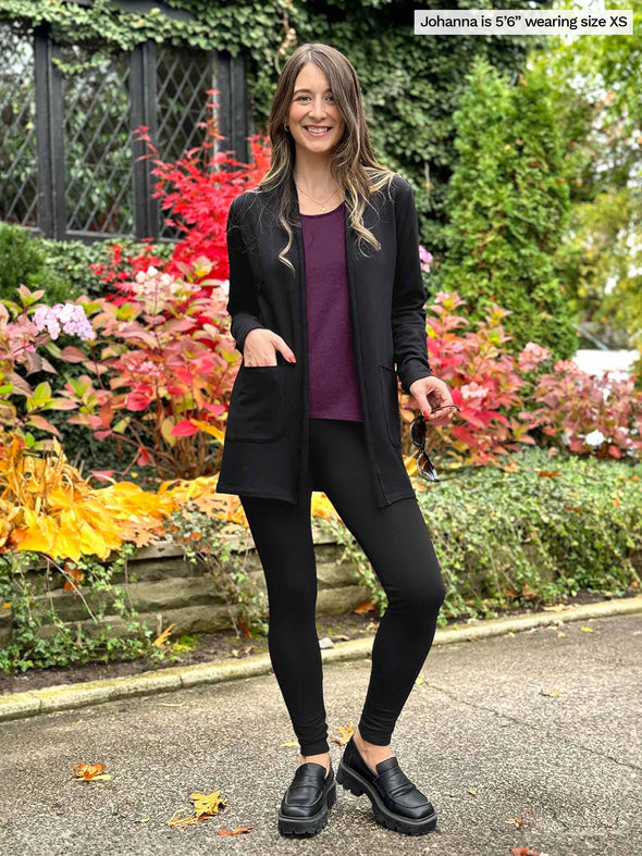 Miik model Jo (5'6, xsmall) smiling wearing Miik's Montana fleece pocket cardigan in black with a matching colour legging and a port  tank