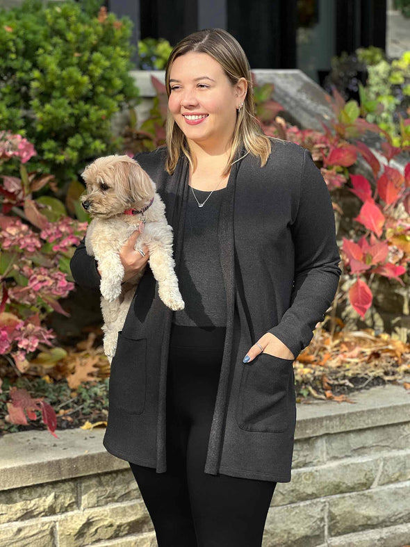 Miik model Christal (5'3", large) smiling and looking away while holding a puppy wearing Miik's Montana fleece pocket cardigan in charcoal with a tank in the same colour and leggings