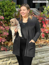 Miik model Christal (5'3", large) smiling and looking away while holding a puppy wearing Miik's Montana fleece pocket cardigan in charcoal with a tank in the same colour and leggings
