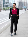 Miik model Meron (5'3", xsmall) smiling wearing Miik's Nala pleated tapered pant in black with a bordeaux collared shirt and a black blazer over her shoulders