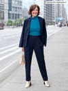Miik founder Donna (5'6", small) smiling and looking away wearing a turtleneck top in teal melange with a navy blazer over her shoulders and Miik's Nala pleated tapered pant in the same colour as the blazer
