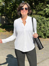 Woman standing outside wearing Miik's Neruda band collar long sleeve shirt in white with grey pants.