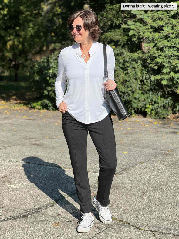 Woman walking wearing Miik's Neruda band collar long sleeve shirt in white with grey pants.