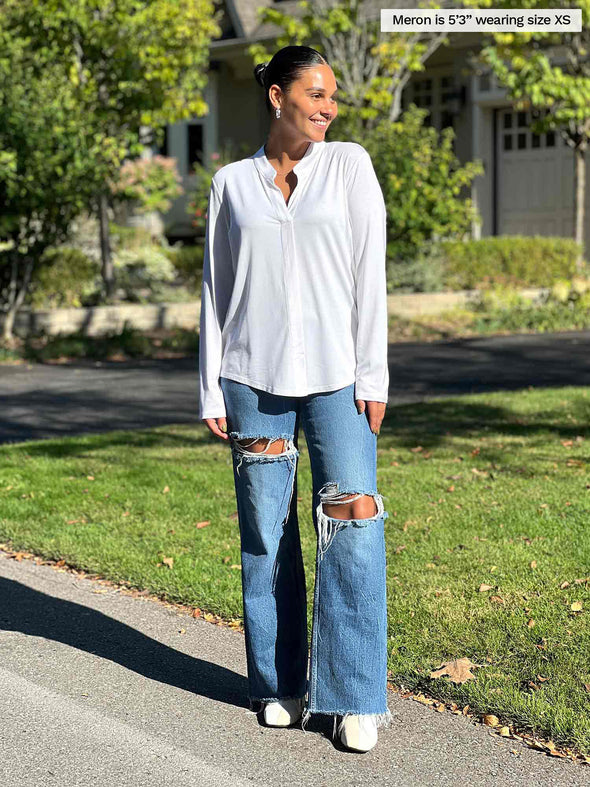Woman standing by a house wearing Miik's Neruda band collar long sleeve shirt in white with jeans.
