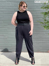 Miik model Bri (five feet five, size xlarge) smiling and looking away wearing Miik's Nida pleat front tapered pant in graphite, a black belt and a tank top in the same colour 