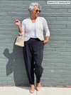 Miik model Keethai (five feet five, size medium) looking away while standing in front of a brick wall wearing a printed cropped cardigan, a white tee with Miik's Nida pleat front tapered pant in graphite
