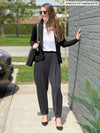 Miik model Johanna (five feet six, size xsmall) standing next to a brick wall wearing Miik's Nida pleat front tapered pant in graphite along with a white collared shirt and a black blazer